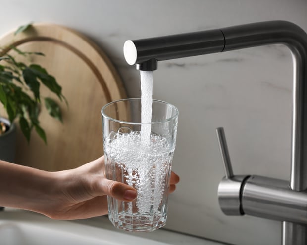 Woman filling glass with water from tap in kitchen