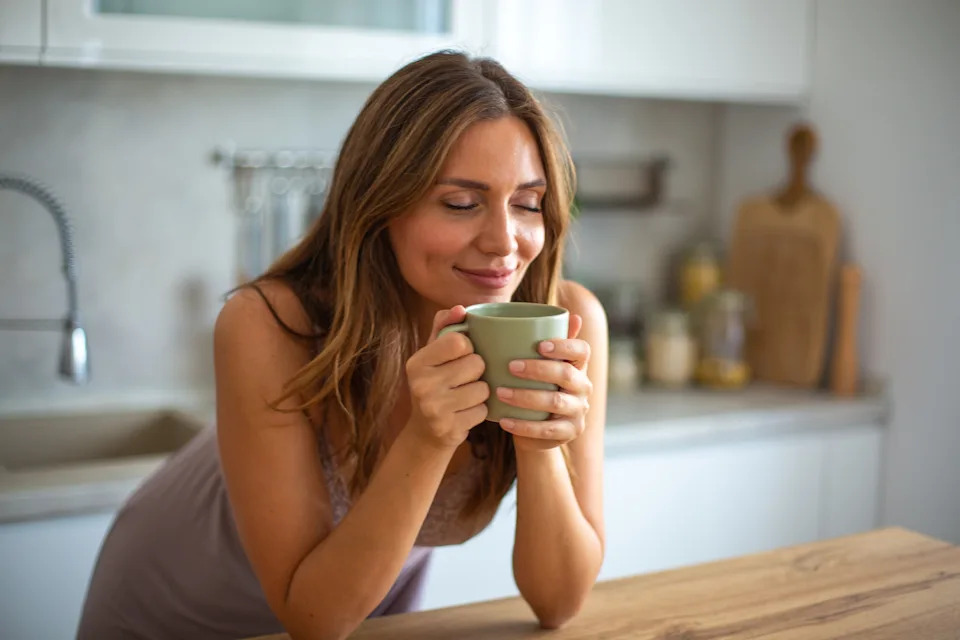 Mid adult woman relaxing in her kitchen, savoring the aroma of a warm beverage
