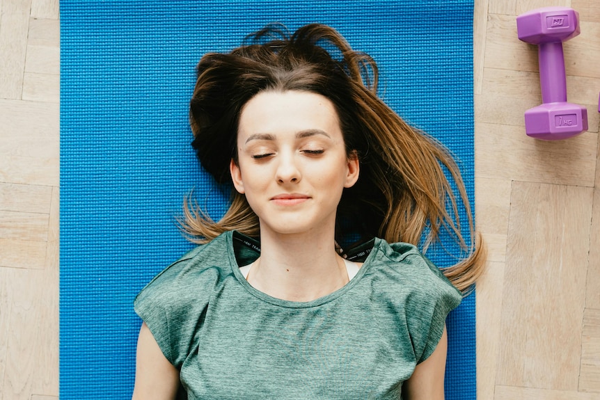 Woman with eyes closed, lying on yoga mat.