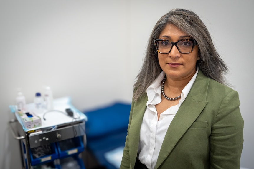 Urologist Ashani Couchman, wearing a white shirt and green jacket, looks at the camera.
