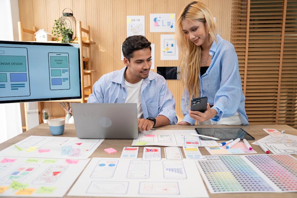 UX/UI designers discussing and brainstorming on wireframes for a website and mobile app prototype, surrounded by sketches of user flow and design tools, in the concept of website and mobile application design concept.