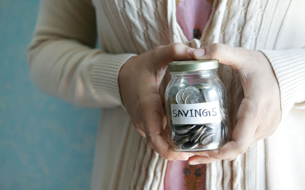 A woman holds a jar of coins labelled savings.