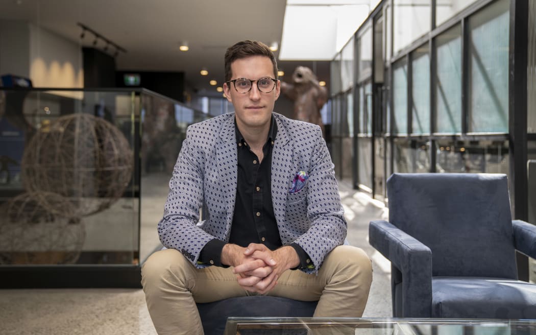 Ed McKnight is a smartly dressed man with glasses sitting with his legs apart on a stool.