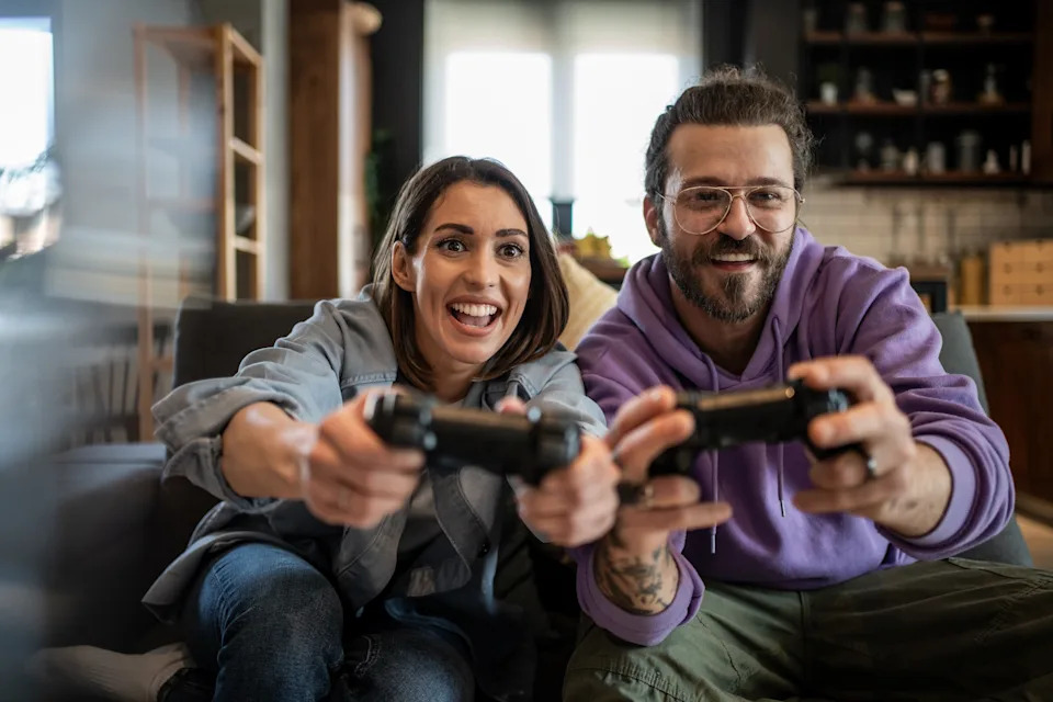 A man and woman smiling and playing video games on a couch, focusing intently on the screen