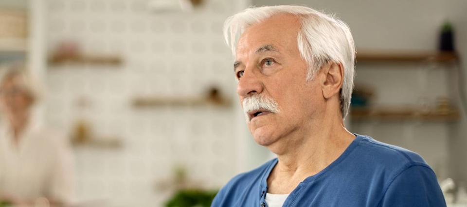 An older man in a blue shirt leans backwards and stares into the middle distance.