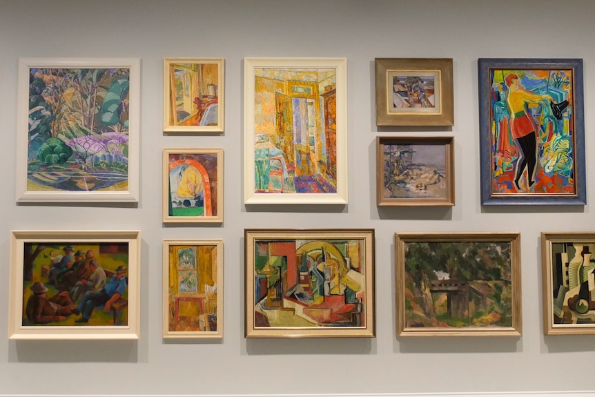 A collection of bright paintings hanging on a gallery wall.