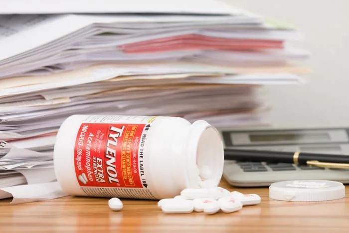 An open Tylenol bottle with pills lies beside a calculator and a stack of paperwork
