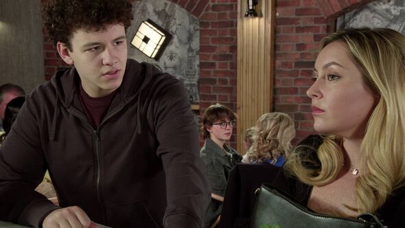 In a room with a brick wall and a golden accent, an individual with a contemplative expression is engaged in a conversation with