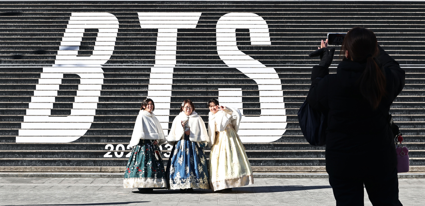 Tourists pose for a photo in front of a promotion for BTS's new album, ″Arirang,″ at the Sejong Center for the Performing Arts in Jongno District, central Seoul, on Jan. 22. [YONHAP] 