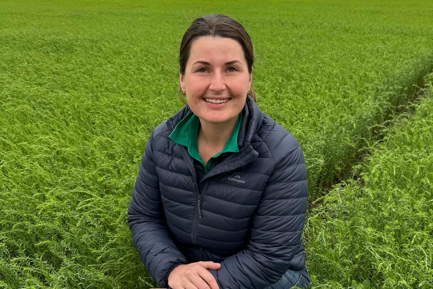 A woman kneels in a lush green crop, smiling to camera