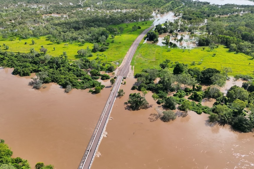 A thin road through a lush and green remote remote area with deep floodwater on either side.