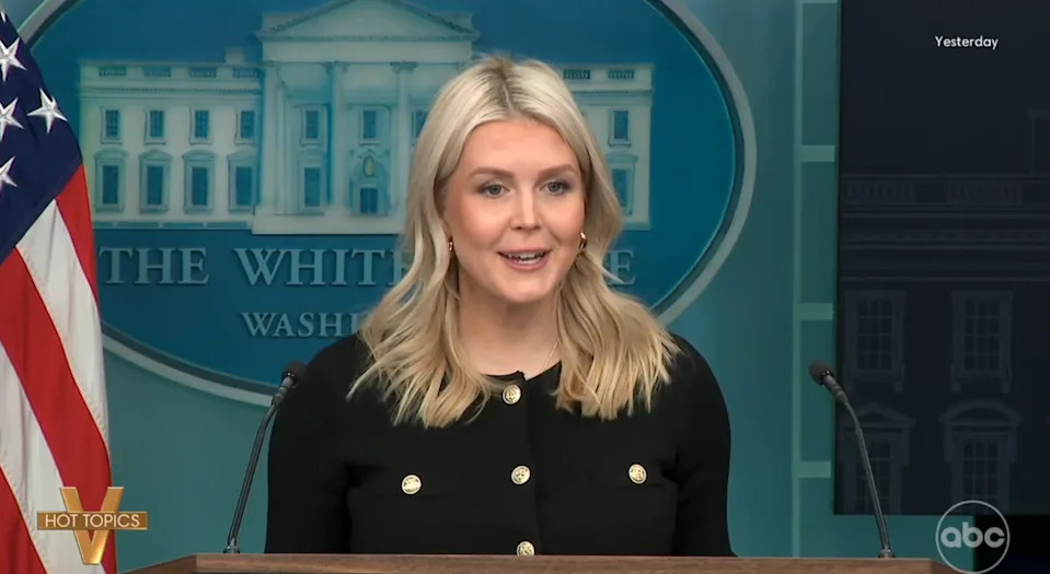 Person speaking at a podium in front of a White House backdrop, with an American flag visible