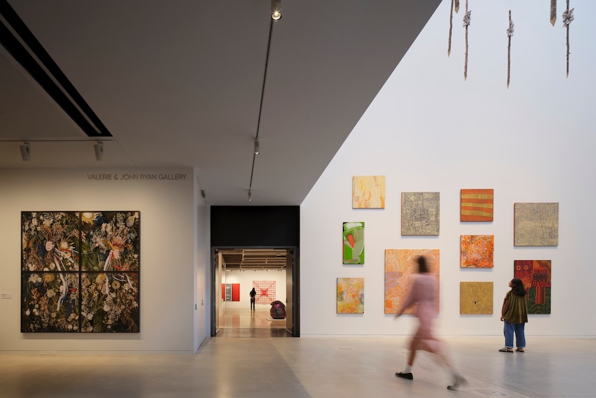 The inside of an art gallery with bright Indigenous art on the walls and people walking past