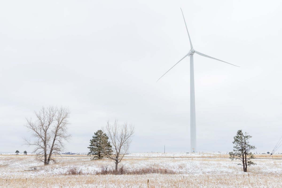 A wind turbine is barely visible against low clouds at NREL. There are trees in front of the tower.