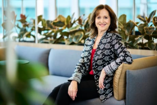 A smiling, dark-haired woman sits on a couch.
