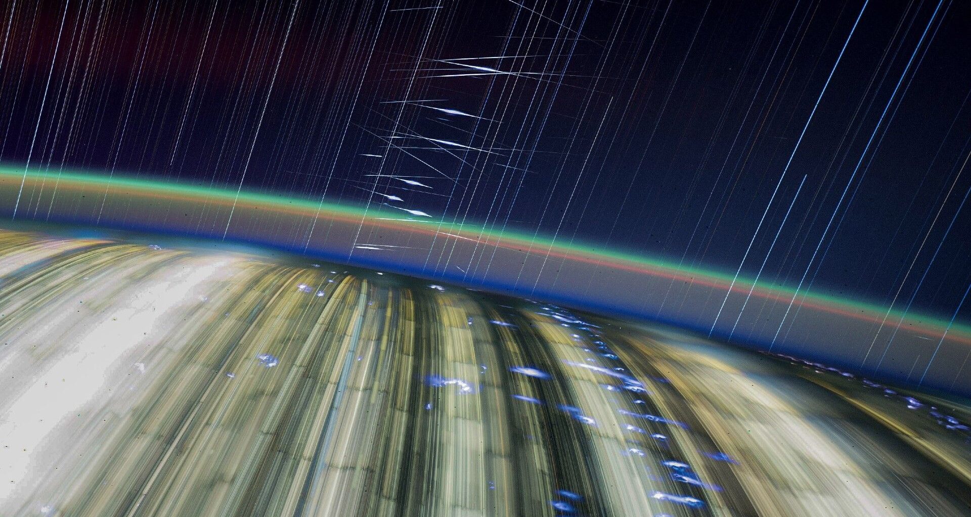 streaks of light crisscross a dark blue sky above a blurry earth below