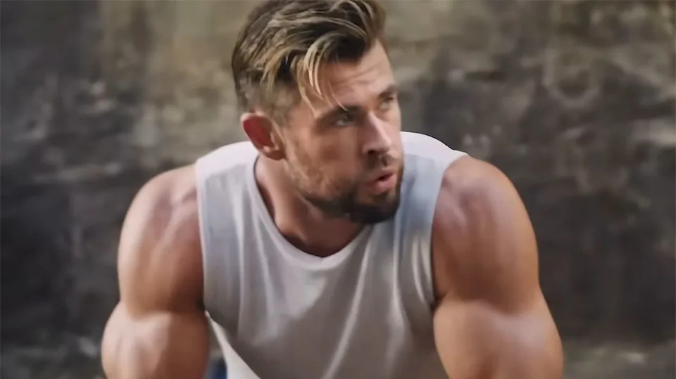  Chris Hemsworth looks to the right in a clip from a Centr ad. He's wearing a white tank and his arms are pumped up. 