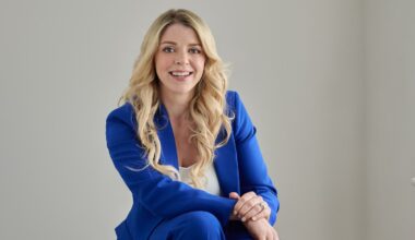 A young white blond woman in a blue suit and white shirt against a grey background.