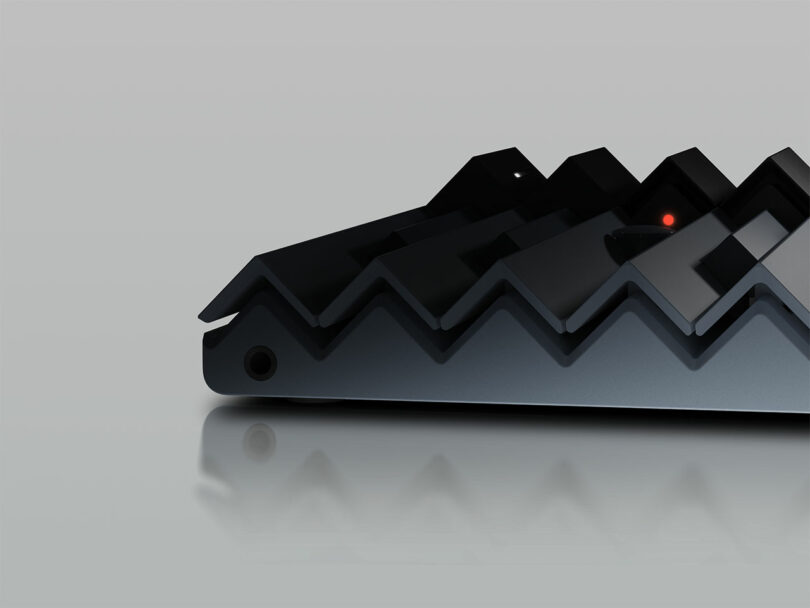 Close-up of a black, zigzag-patterned electronic device with a small red indicator light, placed on a reflective surface.