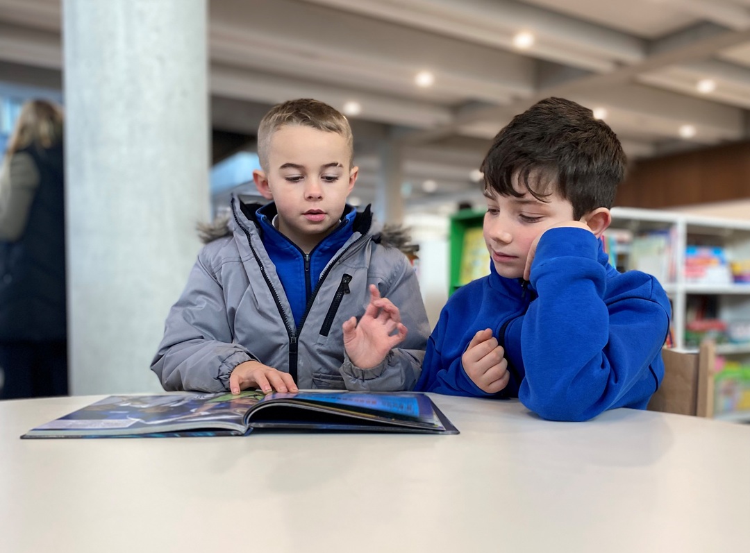 Two young children reading a book in a library.
