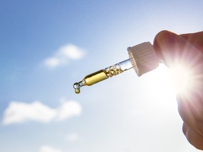 Hand holding dropper pipette with nice golden liquid D-vitamin against sun and blue sky on sunny day. Vitamin D keeps you healthy while lack of sun in winter, cure concept.