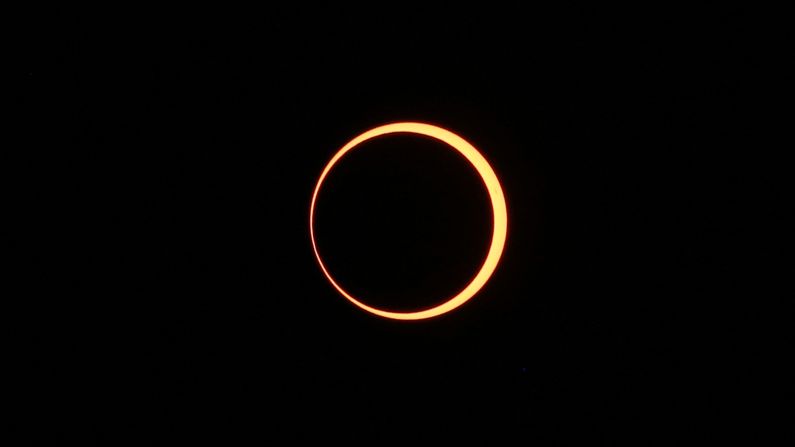 The outline of the sun is visible surrounding the moon during a solar eclipse, with a small break in the circle to the lower left.