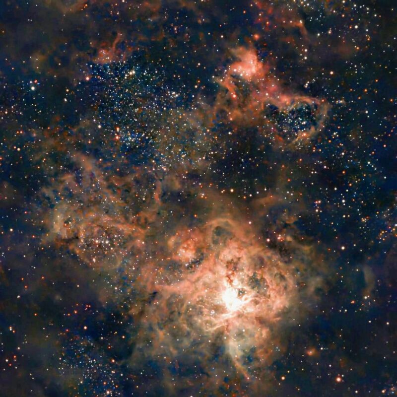 A complex structure of orange gas overlaid with dark nebulae, with numerous background stars.
