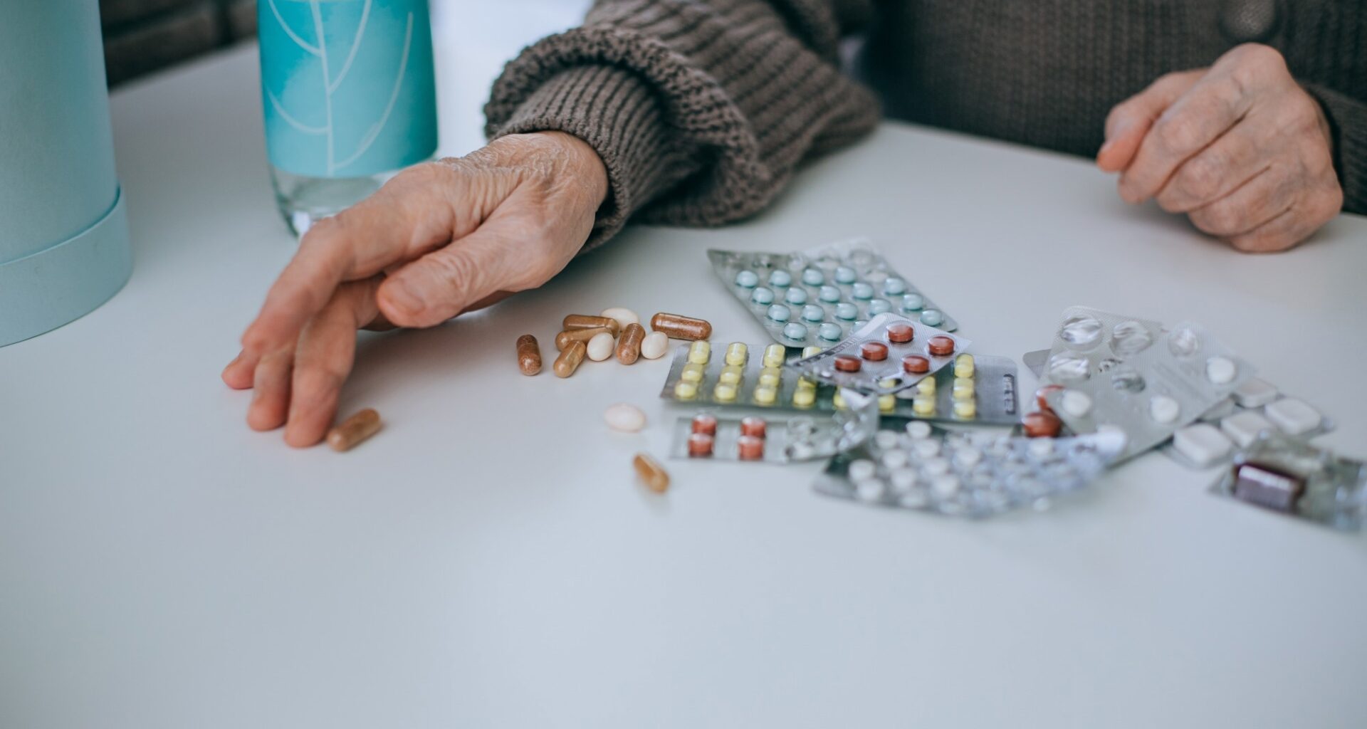 older adult hands next to lots of packets of tablet medication
