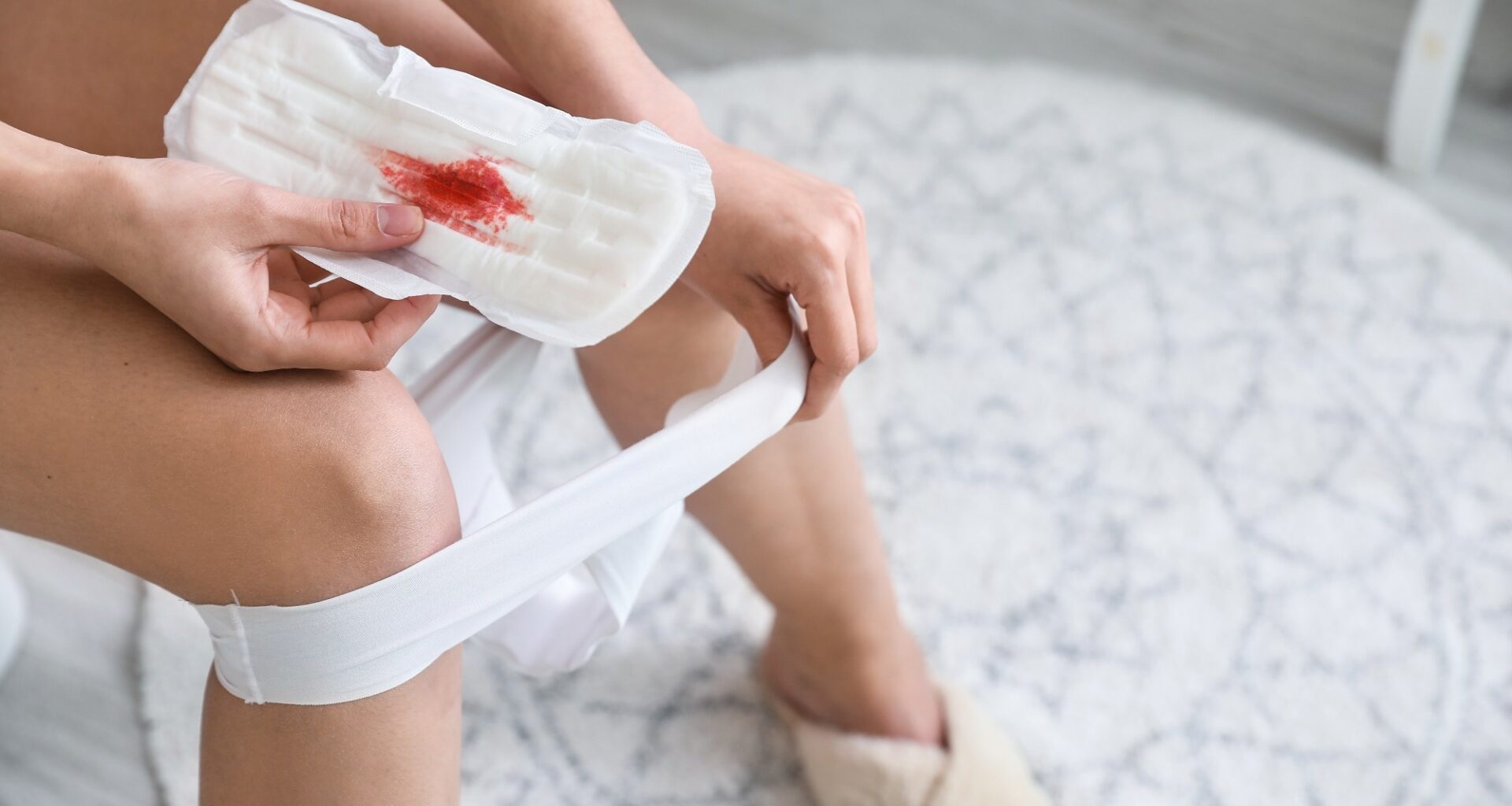Young woman with used menstrual pad sitting on toilet bowl in bathroom,