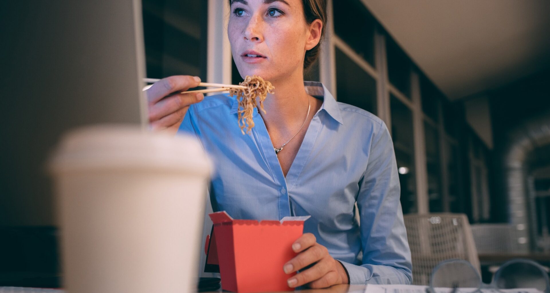 Businesswoman sitting working in office late in the nightre and eating noodles sitting at her desk.