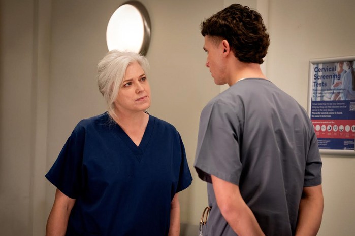 Caroline Harker as Doctor Todd in Emmerdale, wearing hospital scrubs and looking at Joe Warren Plant as Jacob Sugden, who is wearing a grey t-shirt.