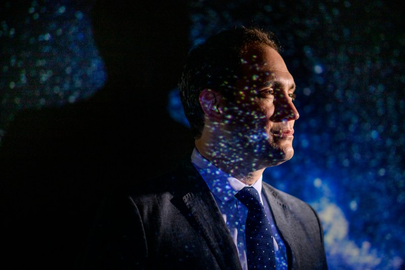 Jonathan Blazek, Northeastern astrophysicist, stands against a projection of stars.