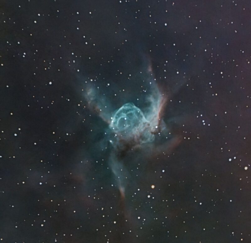 Blue-green H-shaped nebula with reddish wisps and faint background stars.