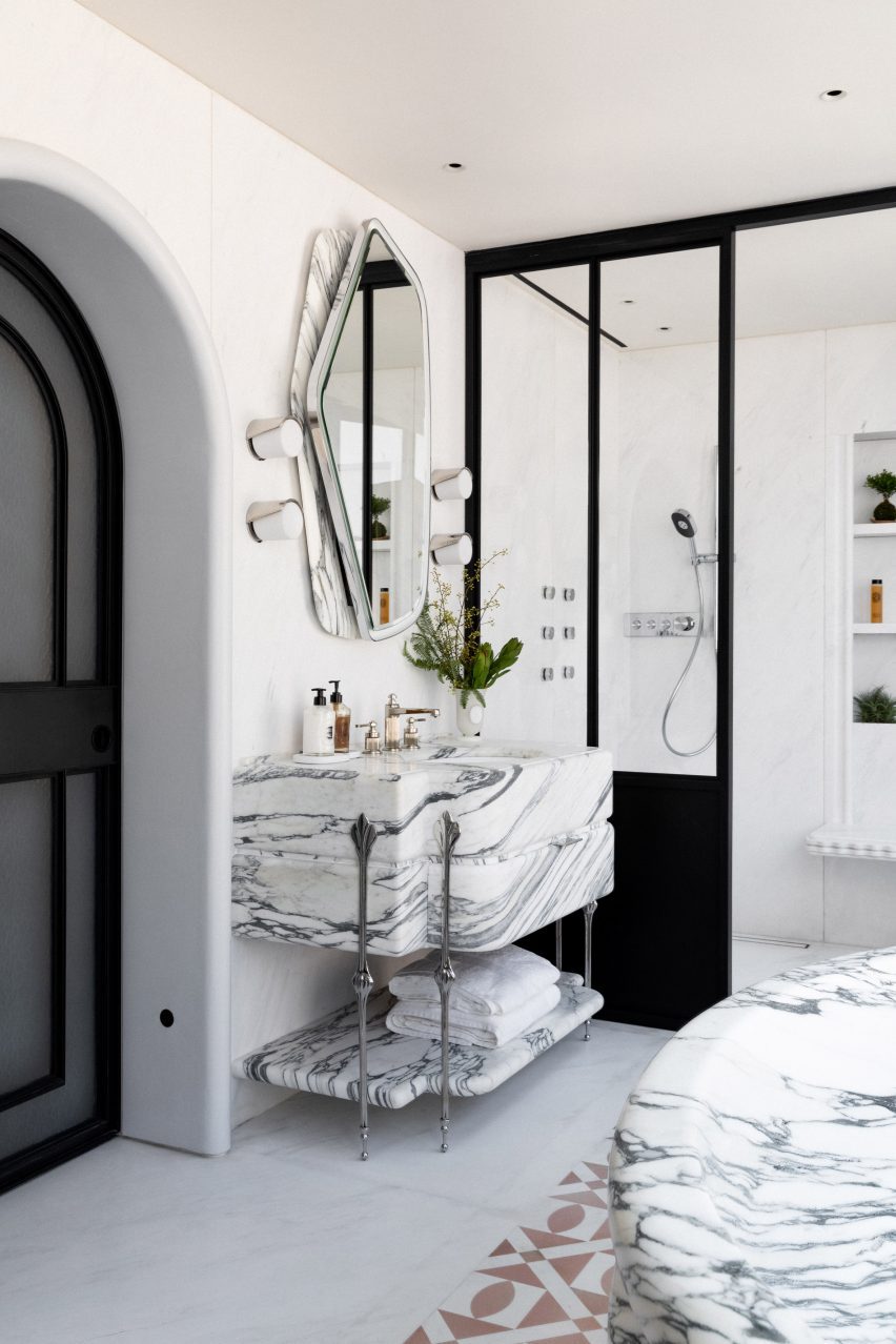 A light bathroom displaying a large, marble sink unit and a shower at the back of the room.