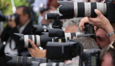 A group of photographers closely packed together, aiming large cameras with telephoto lenses, capturing images at an outdoor event.