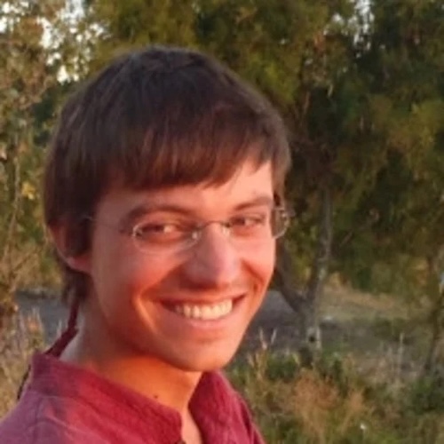 Smiling young man wearing eyeglasses, with trees behind him.