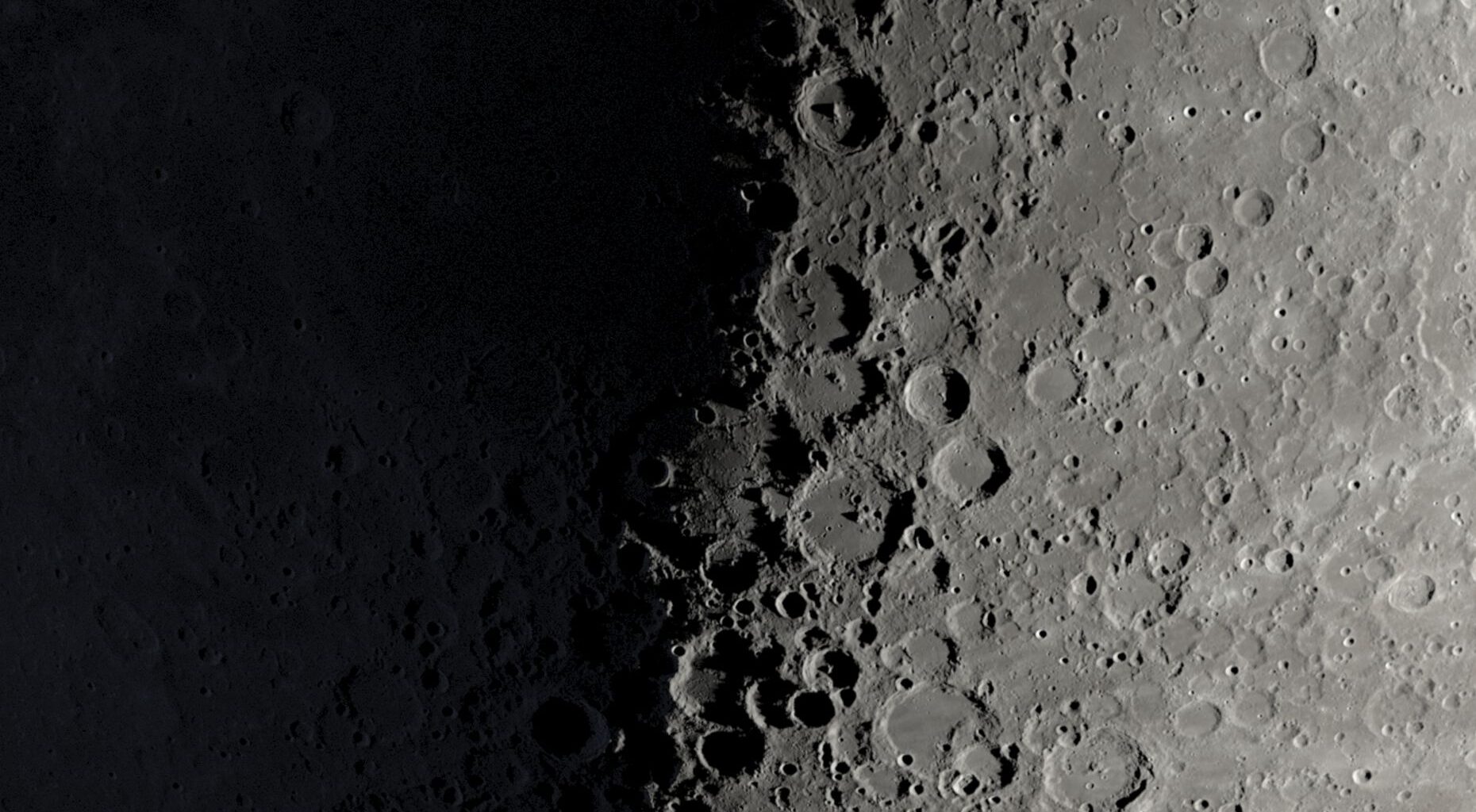 A NASA graphic showing a part of the moon's surface around its first quarter phase when its right half is lit by the sun and its left is in shadow. Large craters can be seen lining the night-day divide.