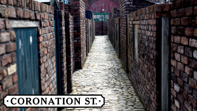 The Coronation Street ginnel with the soap's logo beside it.