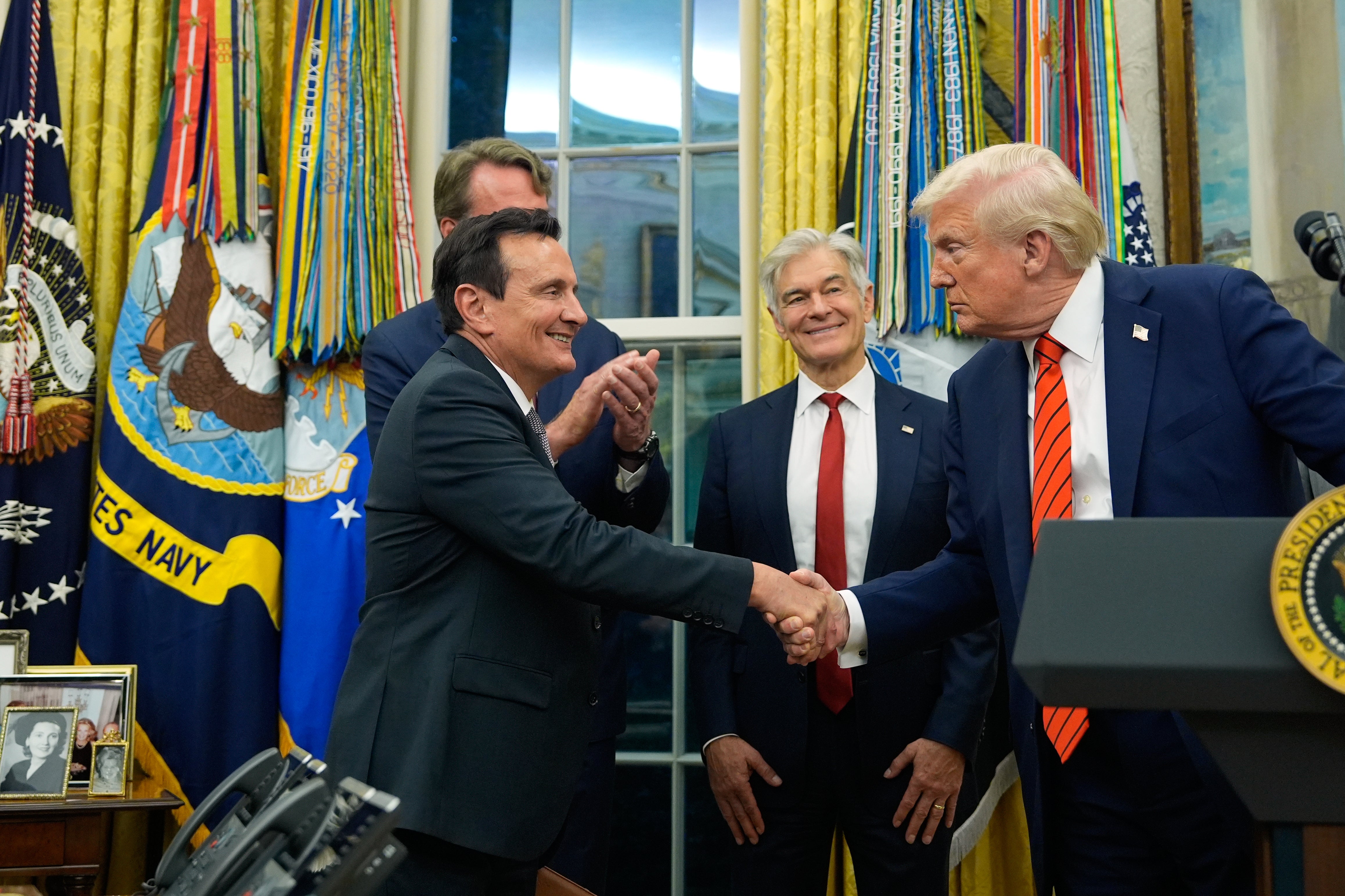 President Donald Trump shakes hands with AstraZeneca CEO Pascal Soriot in the Oval Office of the White House, Friday, Oct. 10, 2025, in Washington, as Virginia Gov. Glenn Youngkin and Centers for Medicare & Medicaid Services administrator Dr. Mehmet Oz watch.