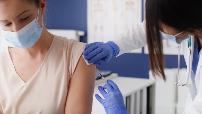 Doctor giving a vaccine injection to an adult woman in a clinic setting