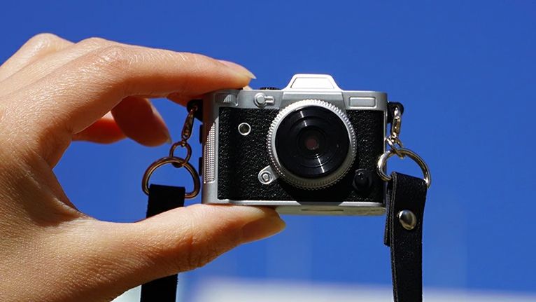 Haru Mini Retro camera being held by fingertips in front of a blue sky