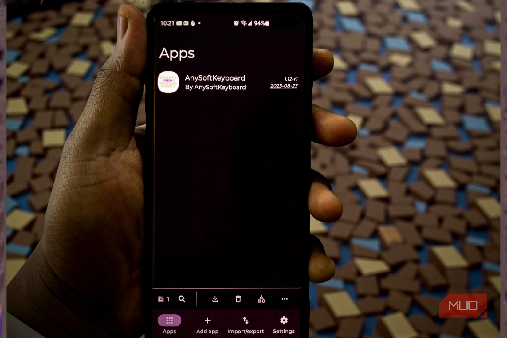 A hand holding a smartphone displaying the Obtainium app dashboard with AnySoftKeyboard listed-1