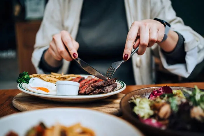 Person dining with steak, fries, and salad at a restaurant, focused on their meal, suggesting a work-related lunch or discussion setting