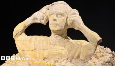 A sculpture of a man putting on ear defenders is made out of plaster.