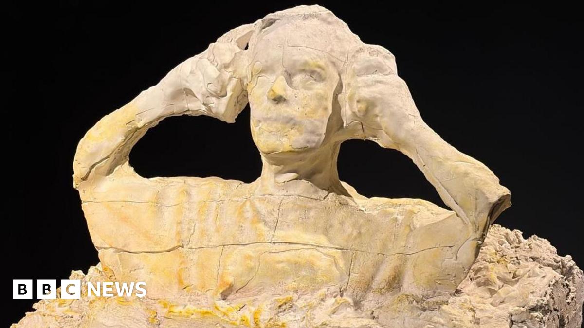 A sculpture of a man putting on ear defenders is made out of plaster.