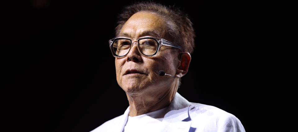 Robert Kiyosaki stands on stage in a pure white suit.