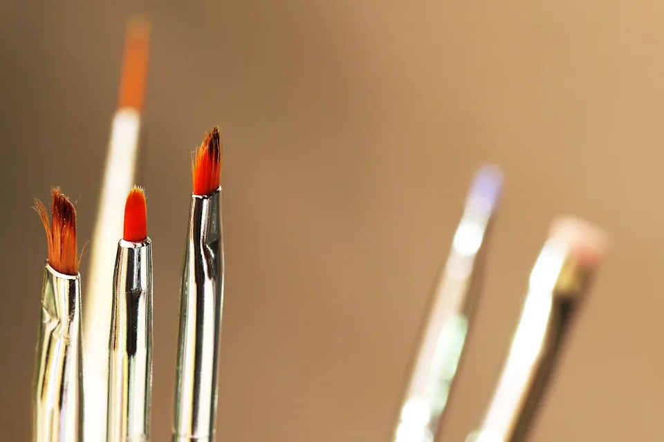 Paintbrushes with various tip shapes and sizes stand upright, ready for use