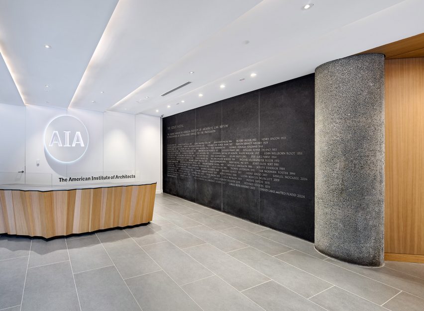 Beside a faceted reception desk, a dark stone wall is inscribed with all winners of the AIA Gold Medal