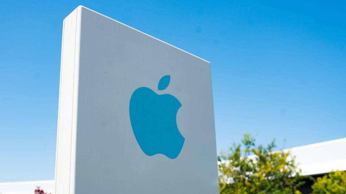 A bright blue Apple logo appears on a sign in front of its California headquarters