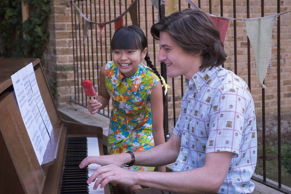 april mae hoang and max macmillan as may tang and timothy turner in call the midwife. timothy playing the piano for his younger sister who smiles.